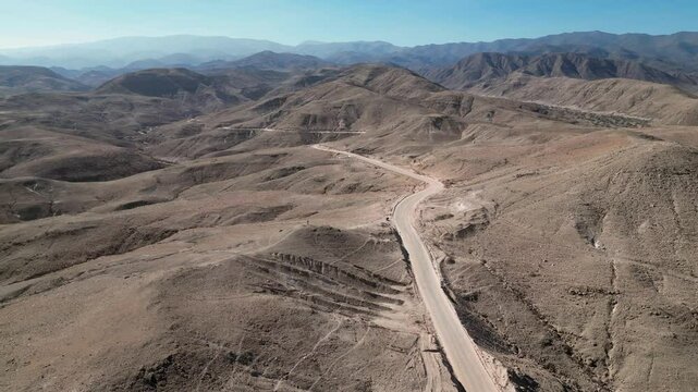 Aerial view: Gravel road cuts through arid foothill mountains in Peru