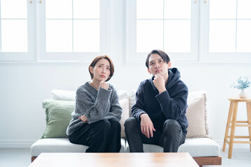 ソファに座り困った表情で考えるカップル