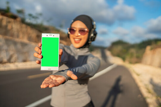 sporty hijab female presenting green screen phone for mockup or advertisement - Powered by Adobe