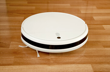 White wireless robot vacuum cleaner on wooden floor in sunlight