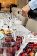 Man pouring champagne from a bottle into a glass. Table with desserts. 