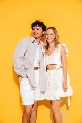 Happy beautiful romantic teenage couple. Smiling handsome caucasian man and young woman in summer clothes posing in studio, hugging sharing emotions, cheerful and happy. Isolated on yellow