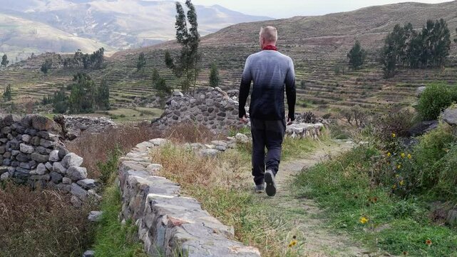 Young Caucasian man walks amid abandoned stone ruins of Uyo Uyo, Peru