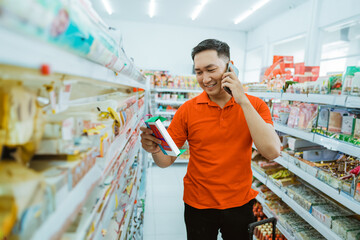 asian male shopper on cell phone holding an item while standing in a minimarket