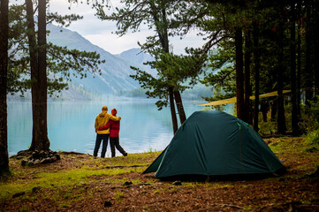 A tourist couple hugs each other standing on the shore of the lake