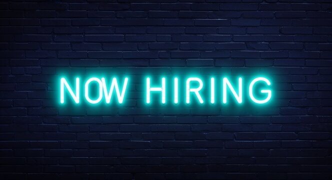 now hiring word lettering glowing with neon light on dark brick wall background
