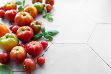Freshly harvested heirloom tomatoes scattered on a beige hexagonal tiled surface with basil leaves