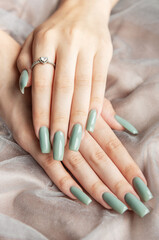 Elegant hands with long green nails resting on soft fabric