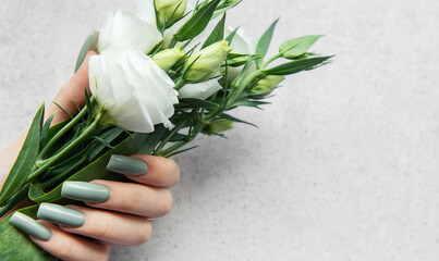 A hand holding a delicate bouquet of white flowers against a soft textured background during...