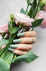 Elegant hand holding a bouquet of pink flowers with soft green nails against a textured gray background