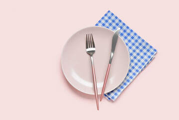 Empty plate, fork and knife on blue checkered napkin on pink background