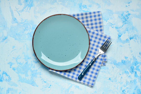 Empty plate, checkered napkin and fork on light blue table