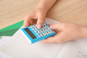 Woman working with calculator on wooden table, closeup