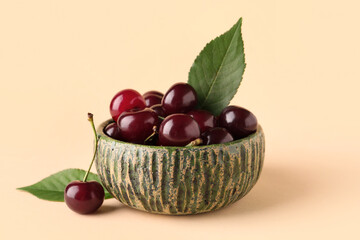 Bowl with sweet cherries and leaves on beige background