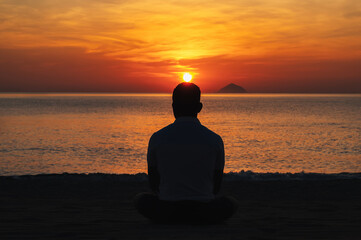 silhouette of a man meditating on the beach by sea in the morning at dawn in summer