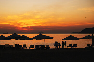 Silhouettes of vacationing tourists and beach umbrellas on the beach by the sea in the evening at sunset in summer at the resort