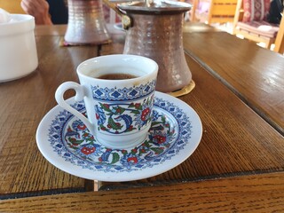 A cup of coffee on the table. Coffee pot in the background.