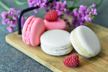 Wooden tray with sweet macaroons and raspberries on dark background
