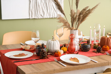 Autumn table setting with pumpkins, dry leaves and burning candles in dining room