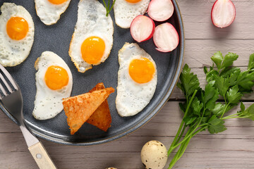 Plate with fried quail eggs, toasts and radish on grey wooden table, closeup