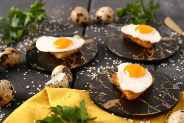 Composition with tasty fried quail eggs, toasts, parsley and sesame seeds on dark wooden background