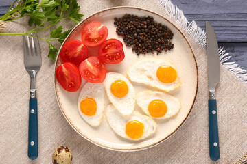 Plate with fried quail eggs, tomatoes, peppercorns and cutlery on table
