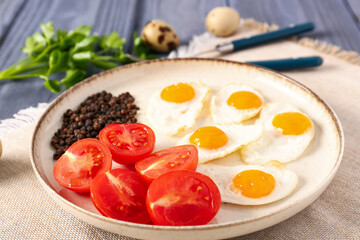 Plate with fried quail eggs, tomatoes and peppercorns on color wooden table, closeup