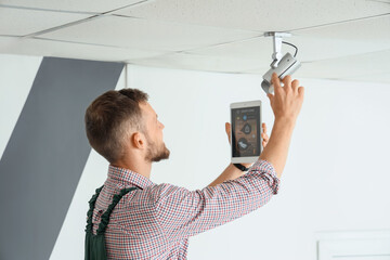 Male worker with tablet computer installing alarm system in room