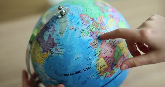 Young person moves index finger over surface of massive globe studying countries and capitals. Student gets knowledge during geography lesson at school