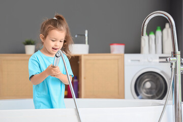 Cute little girl with shower head in bathtub. Child at risk