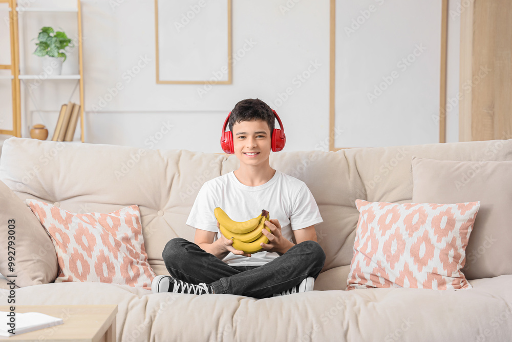 Canvas Prints Teenage boy in headphones with bananas sitting on sofa at home