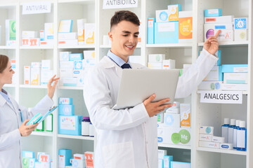 Male pharmacist with laptop showing medications online at pharmacy