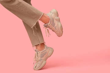 Legs of young woman in stylish beige sneakers on pink background
