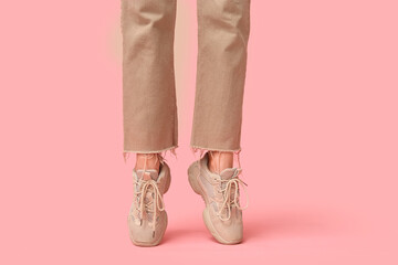 Legs of young woman in stylish beige sneakers on pink background
