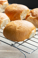 Freshly baked bread rolls cobs cooling down on a cooling rack on a wooden board. Home baking concept