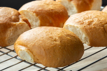 Freshly baked bread rolls cobs cooling down on a cooling rack on a wooden board. Home baking concept