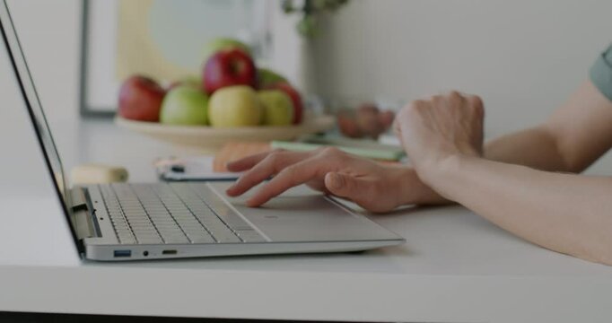 Close-up of female hands typing with laptop while woman freelancer working with computer at kitchen table. Home and business activity concept.