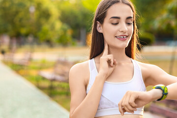 Sporty young woman counting pulse after training in park