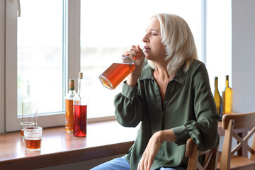 Mature woman drinking whiskey at home. Concept of alcoholism