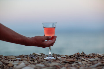 Hand is holding glass with pink vine on the pebbles beach
