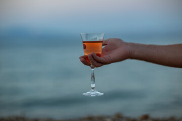 Hand is holding glass with pink vine on the pebbles beach