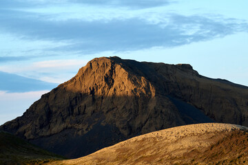 Rocky mountain with sunlight on ridge against cloudy blue sky
