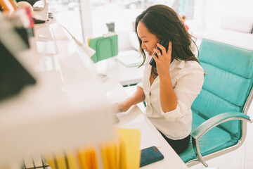 A professional asian woman on the phone in an office. 