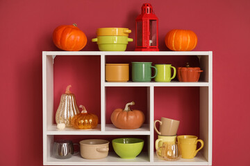 Shelf with different dishes and autumn decor hanging on color wall