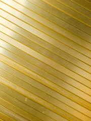 Wall or ceiling covered in diagonal, golden or brass aluminum slats, creating a sleek and modern aesthetic.