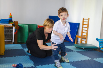 Dedicated therapist assists a young boy with movement disorders as he practices standing, enhancing...