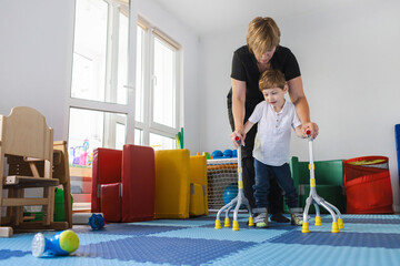 Young boy with musculoskeletal disorders uses assistive rehab canes while practicing walking with...