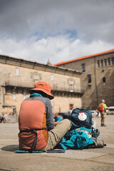 Pilgrim resting in obradoiro square after finishing the camino de santiago, with the backpack and the scallop shell