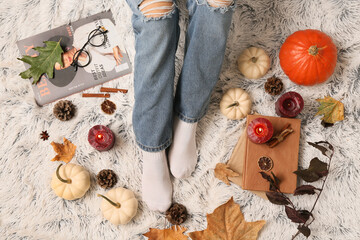 Female legs in warm socks with autumn leaves, candles and pumpkins on white plaid as background