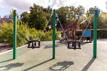 Empty playground in daytime with swings and equipment surrounded by greenery